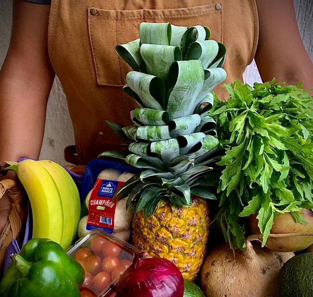Canasta con plátano, piña, cebolla morada, aguacate y verduras frescas